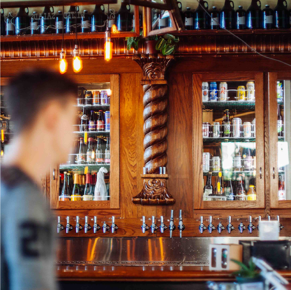 Ornate wooden back bar with carved column, rows of taps and shelves of bottles and cans