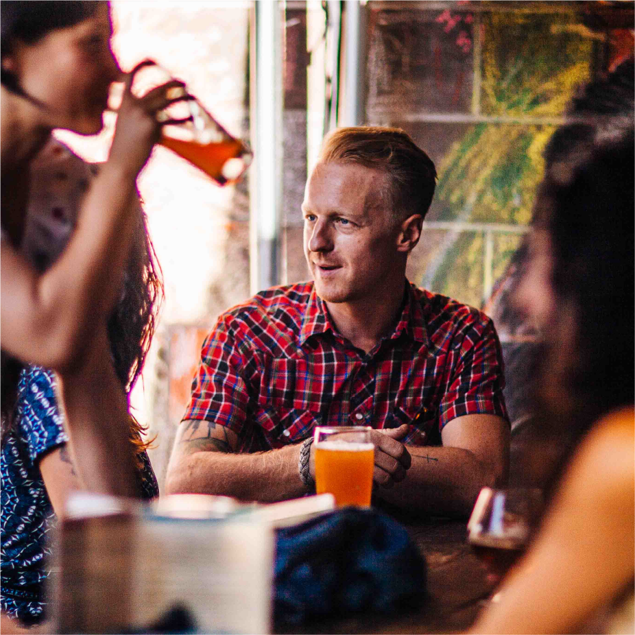Man in a plaid shirt at a bar table talking with friends drinking beer