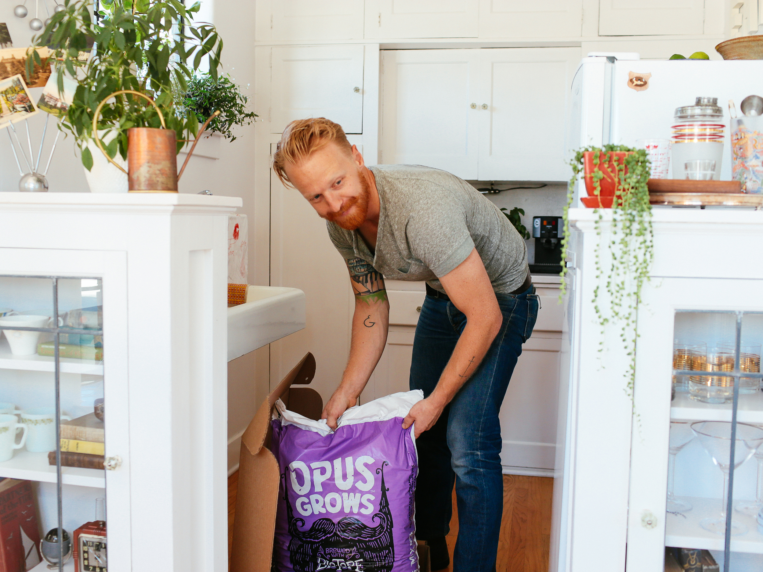 Bearded man in a white kitchen opening a bag of Opus Grows potting soil