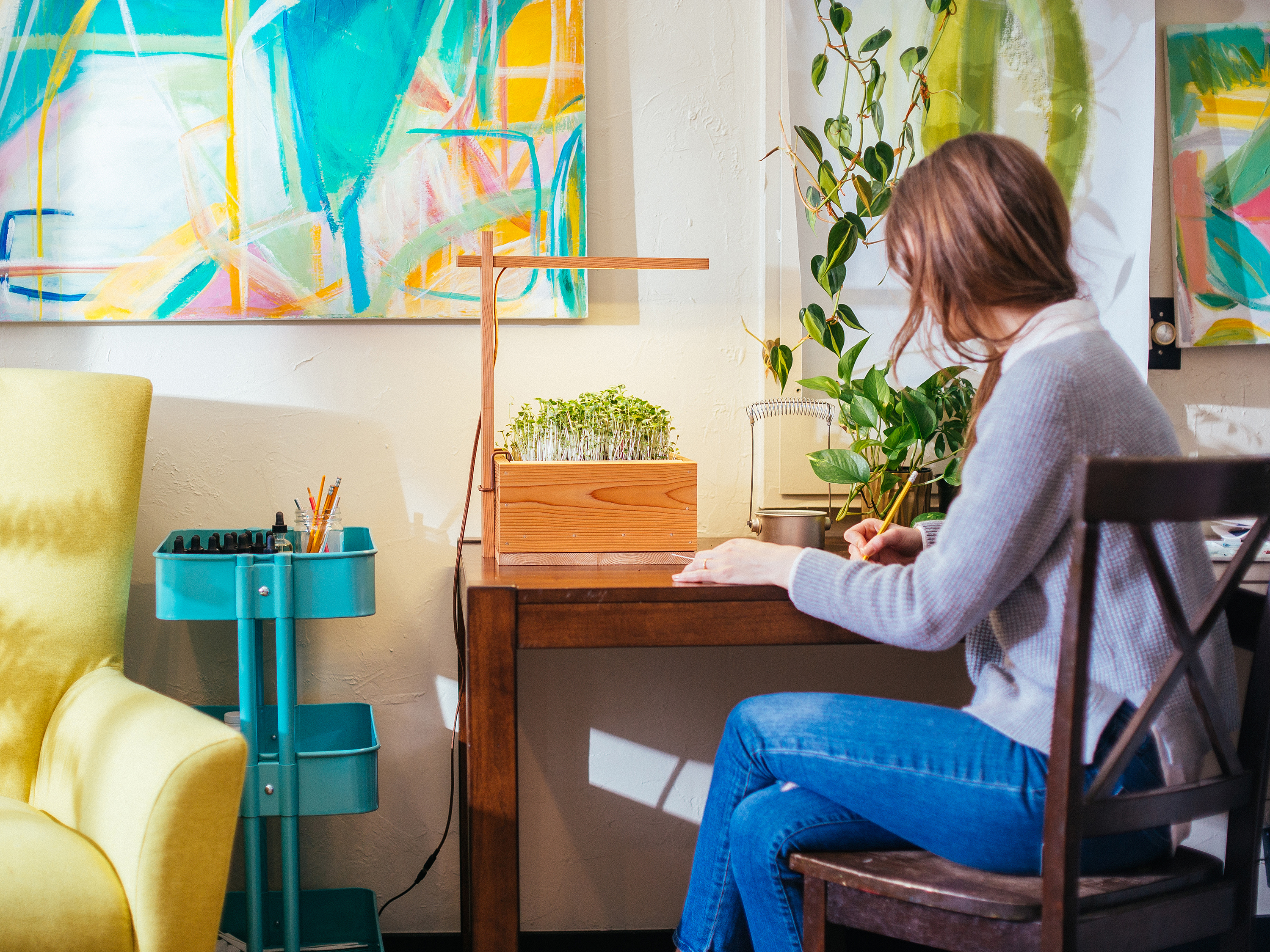 Woman writing at a desk lit by an Opus Grows wooden lamp growing microgreens