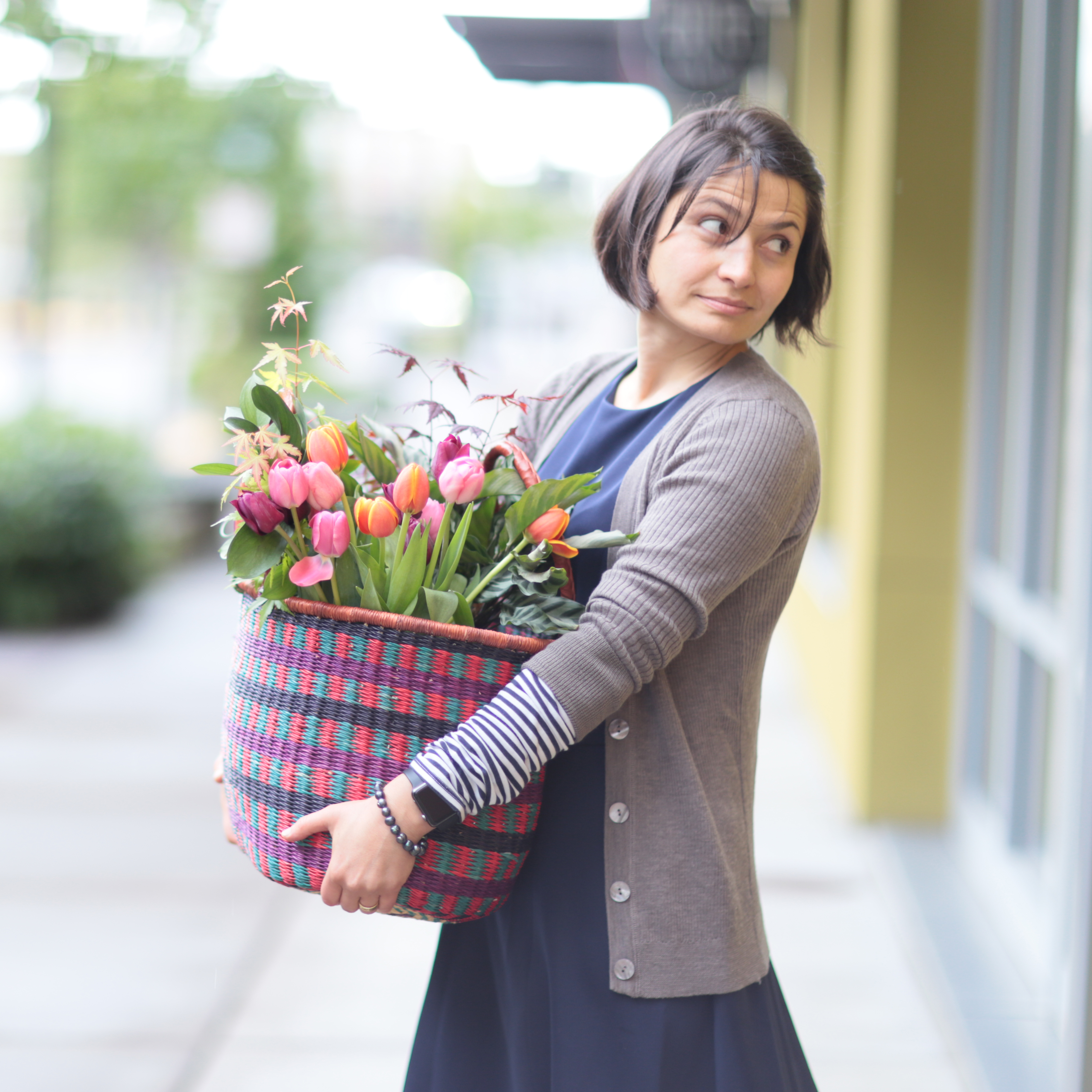 Woman carrying a colorful woven basket full of tulips and flowers on a sidewalk