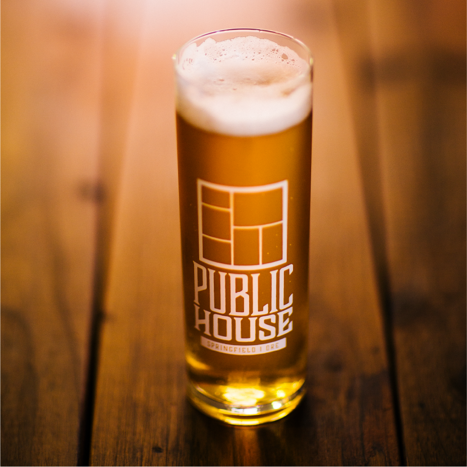 Pint of beer in a glass etched with the Public House Springfield logo on a wood table
