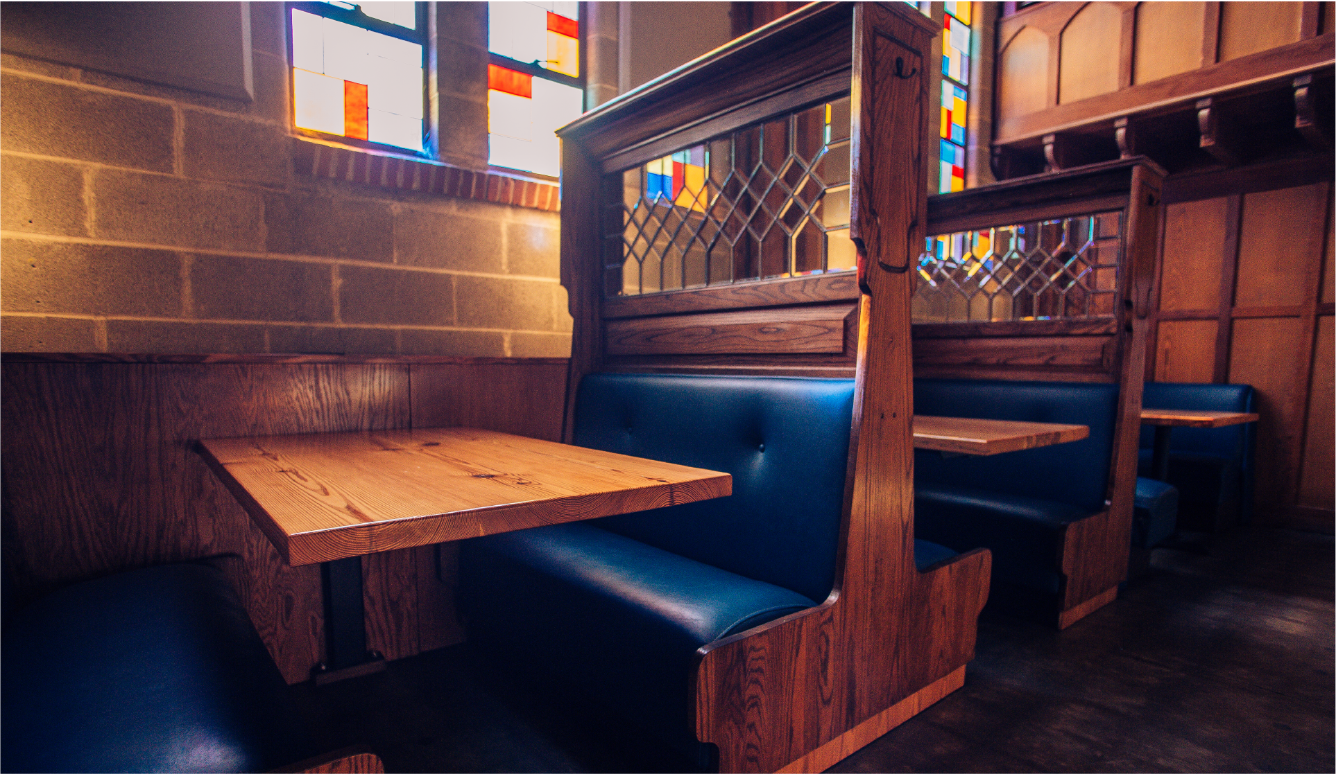 Pub interior with wooden high-back booth benches, blue cushions and stained-glass partitions