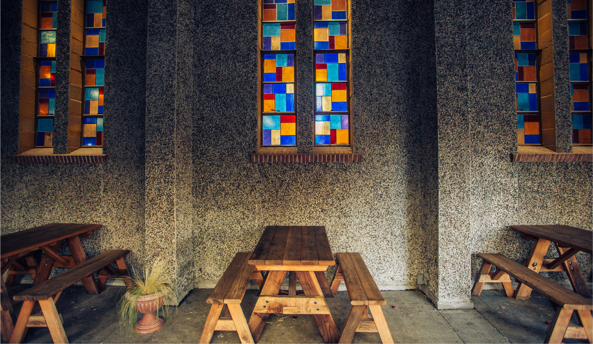 Pub seating with wooden picnic-style tables and benches below colorful stained-glass windows