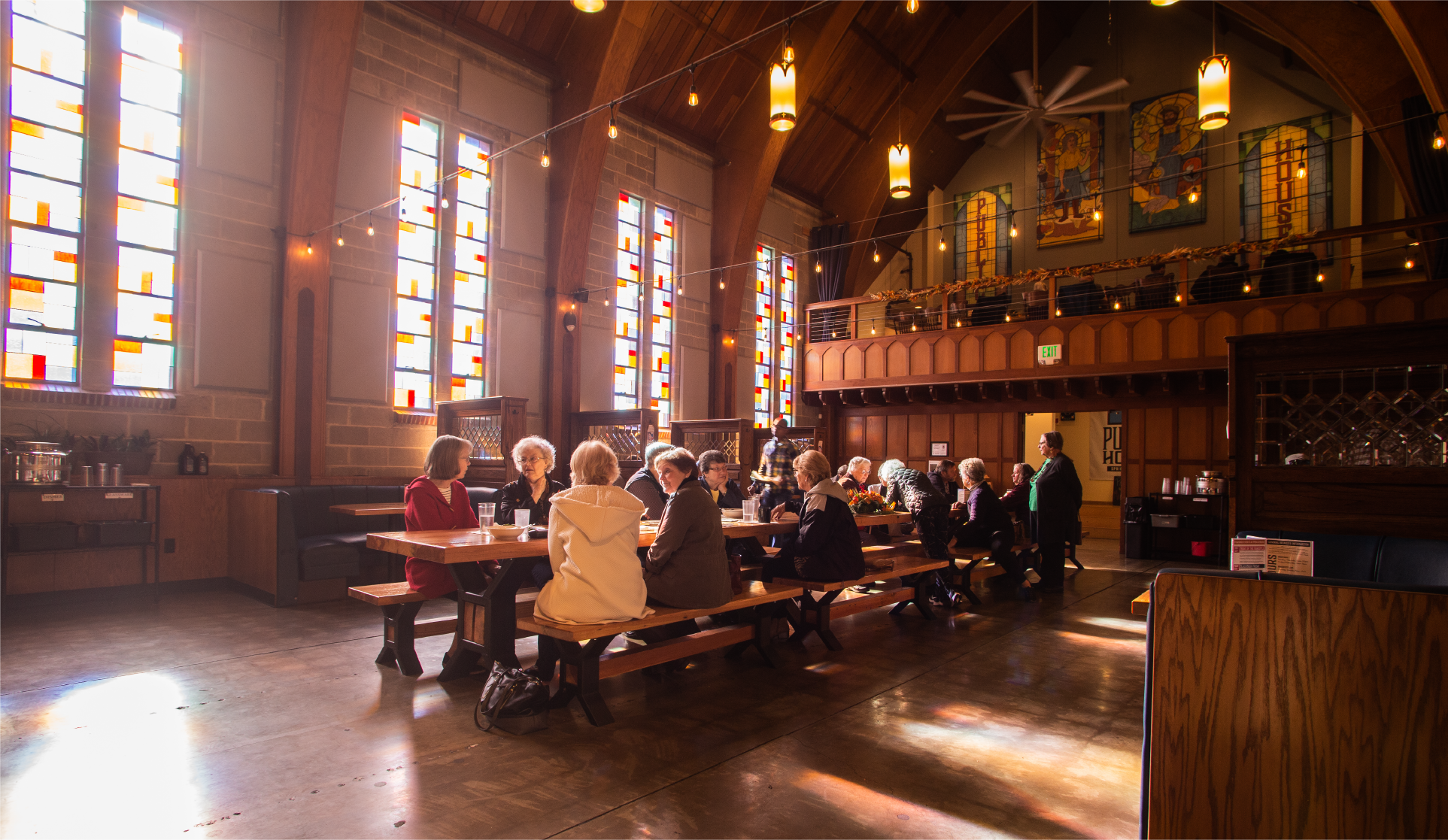 Seniors seated at long tables in a converted church hall with stained-glass windows