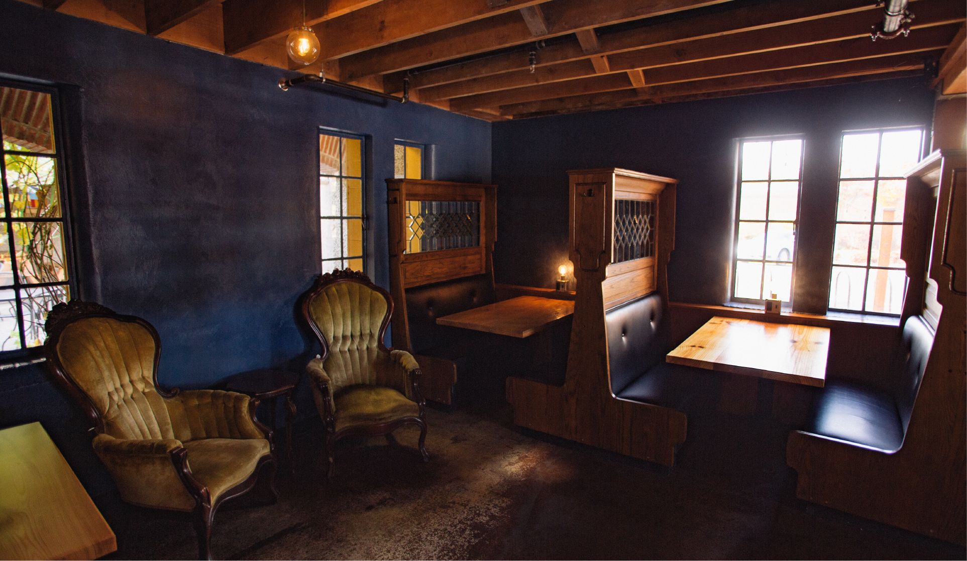 Dim pub interior with dark blue walls, vintage tufted armchairs and wooden high-backed booth seating