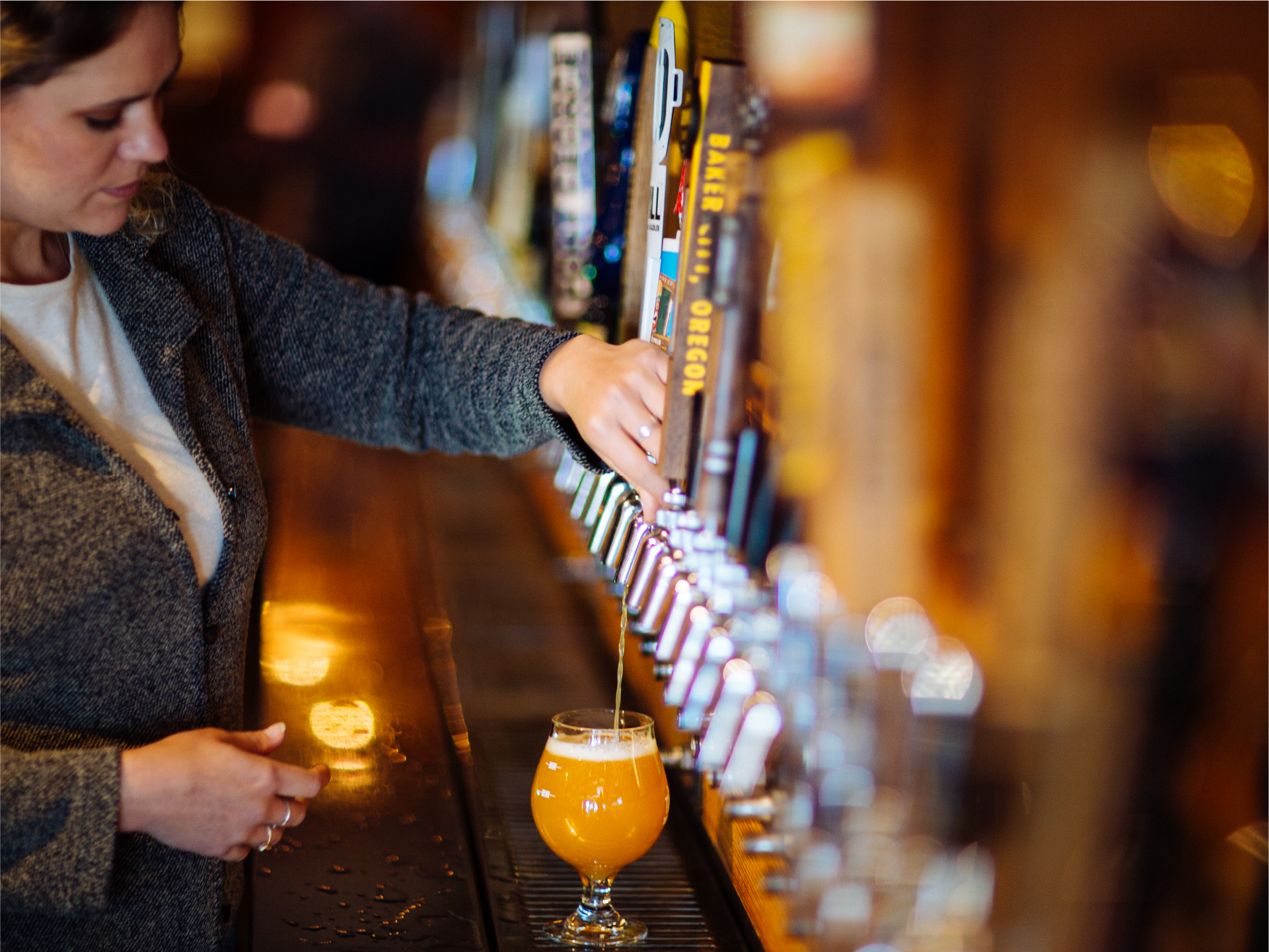 Woman pouring beer from a tap into a glass at a bar with many tap handles