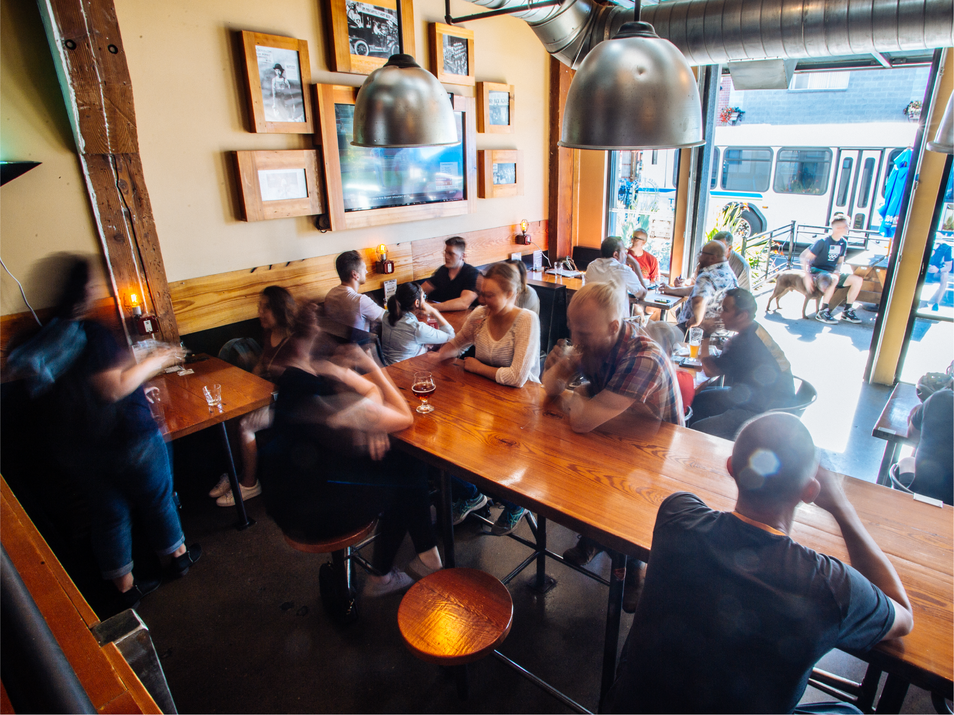 People seated at long communal tables in a pub with framed photos and an open garage door