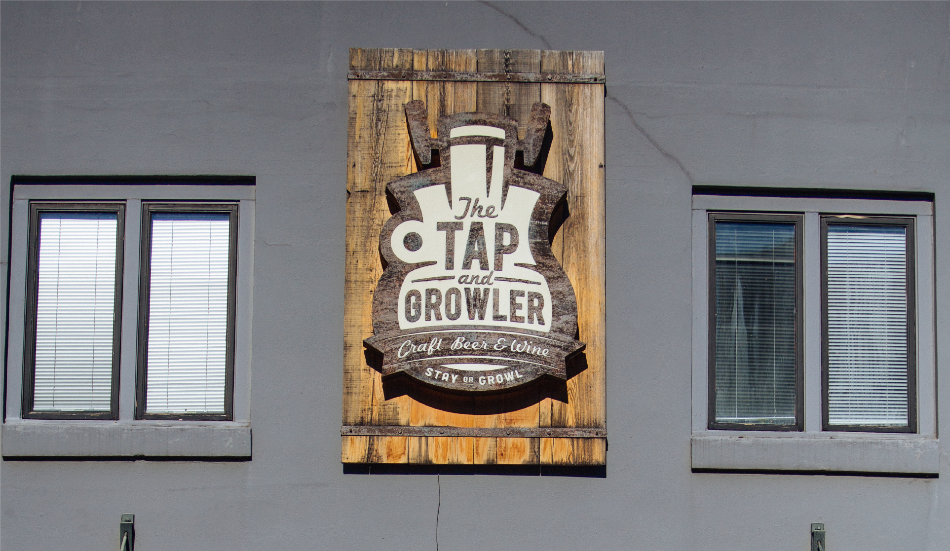 Carved wood sign for The Tap and Growler Craft Beer and Wine mounted on a gray building wall