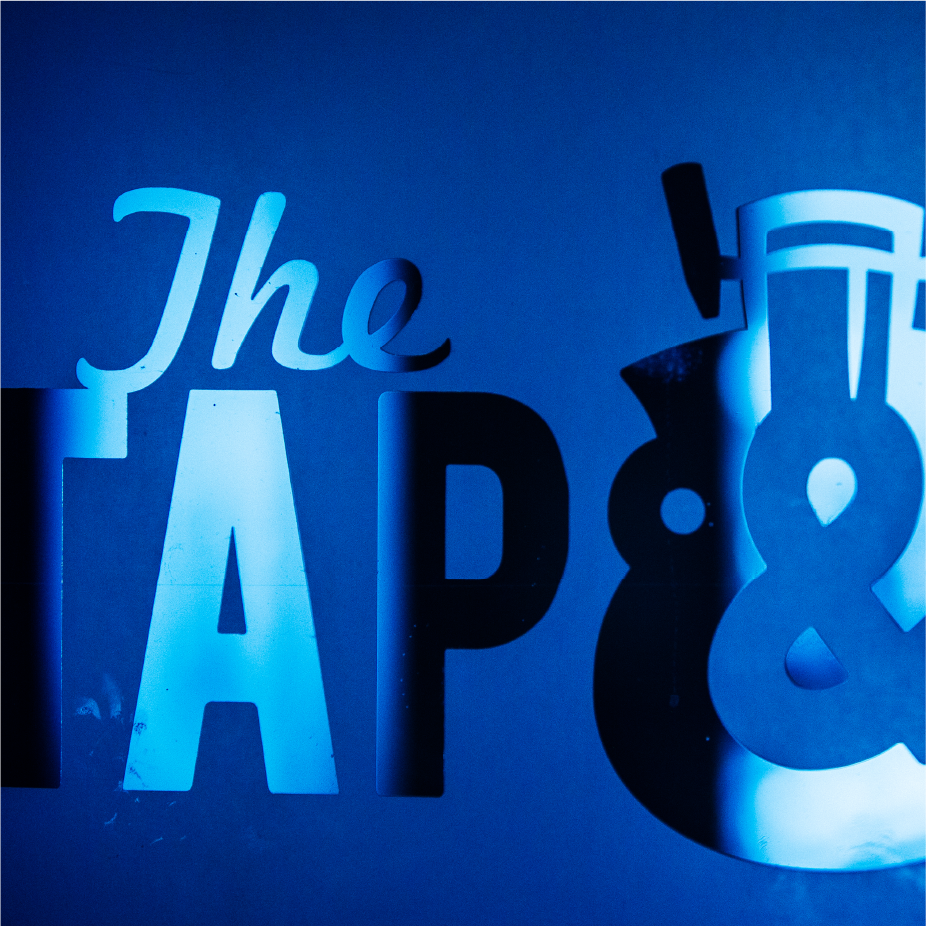 Cut-metal "The Tap &" signage lit in deep blue light