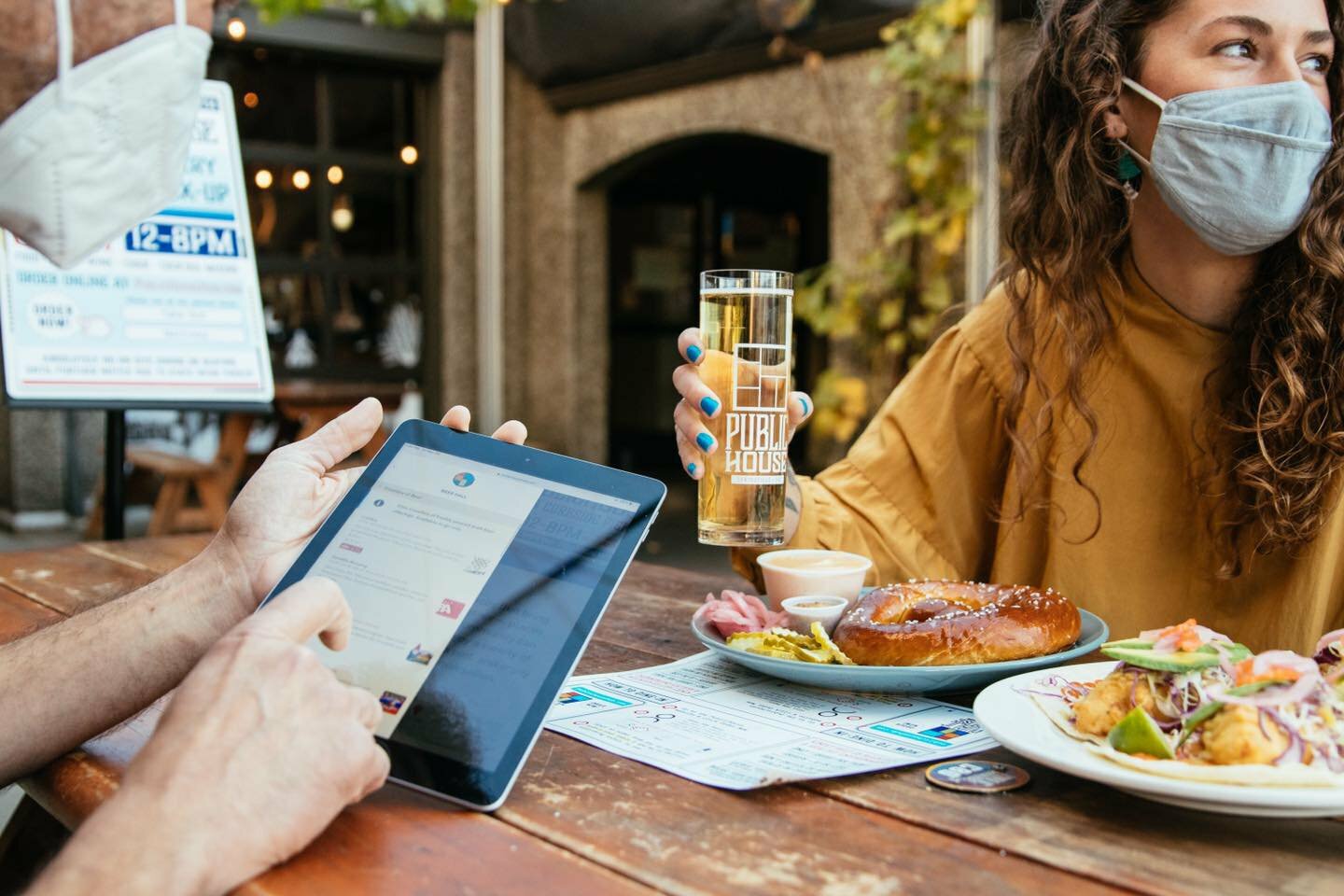 Diner holding a Public House beer glass while a server presents a tablet at an outdoor table