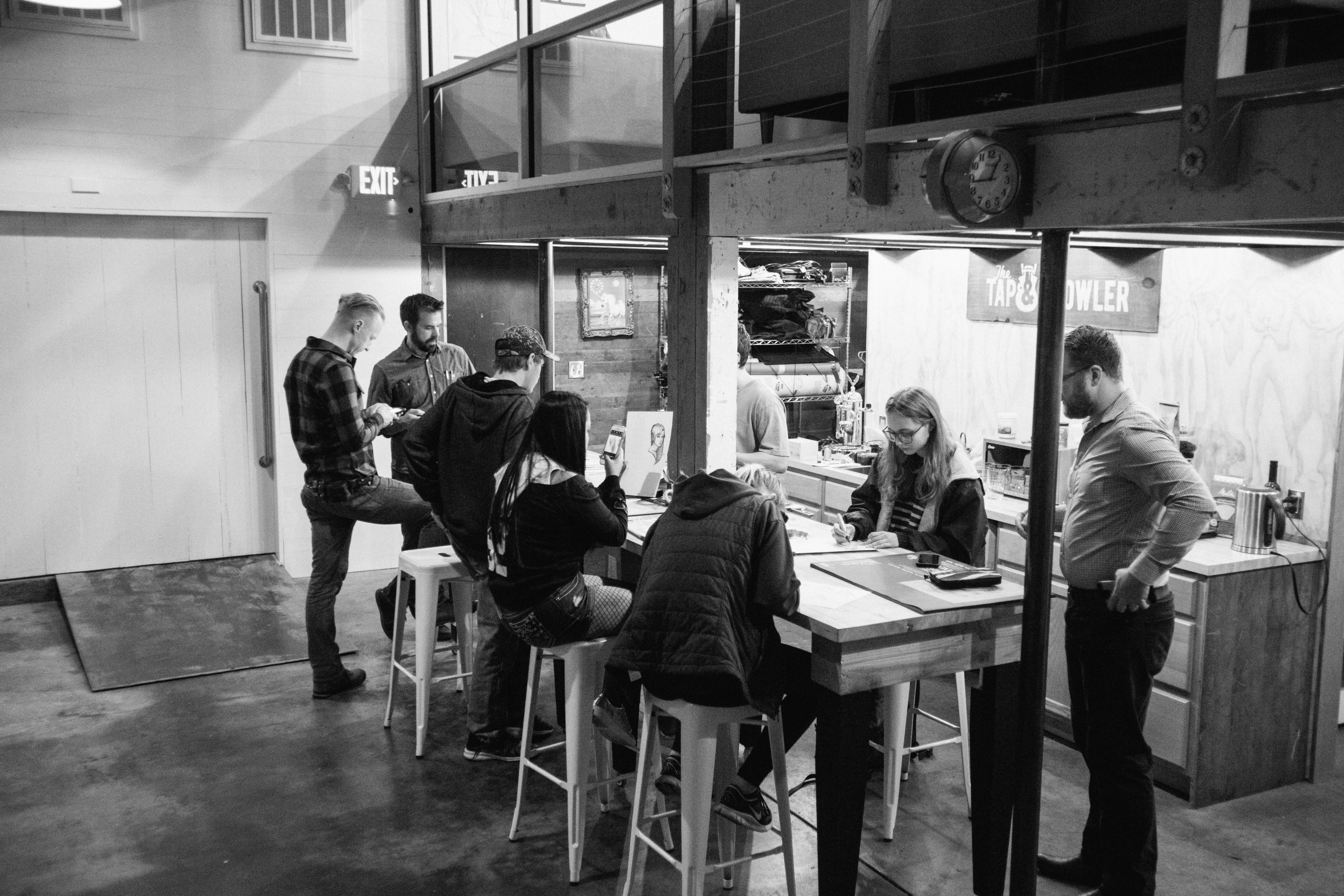 People gathered at high tables for a Lane Arts Council design workshop in a warehouse space, black and white
