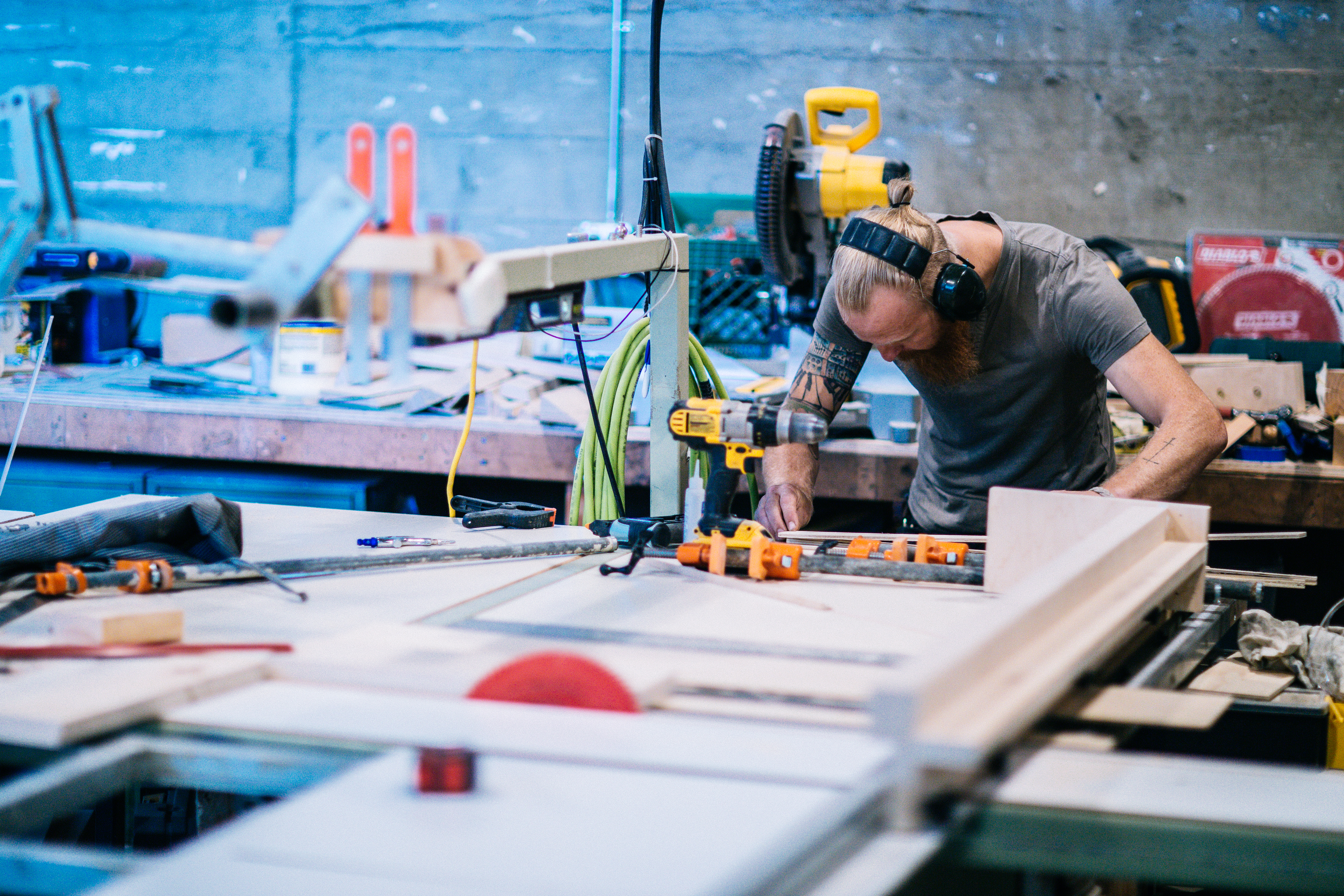 Man with ear protection using a drill to assemble a booth on a workshop table, Drawn fabrication