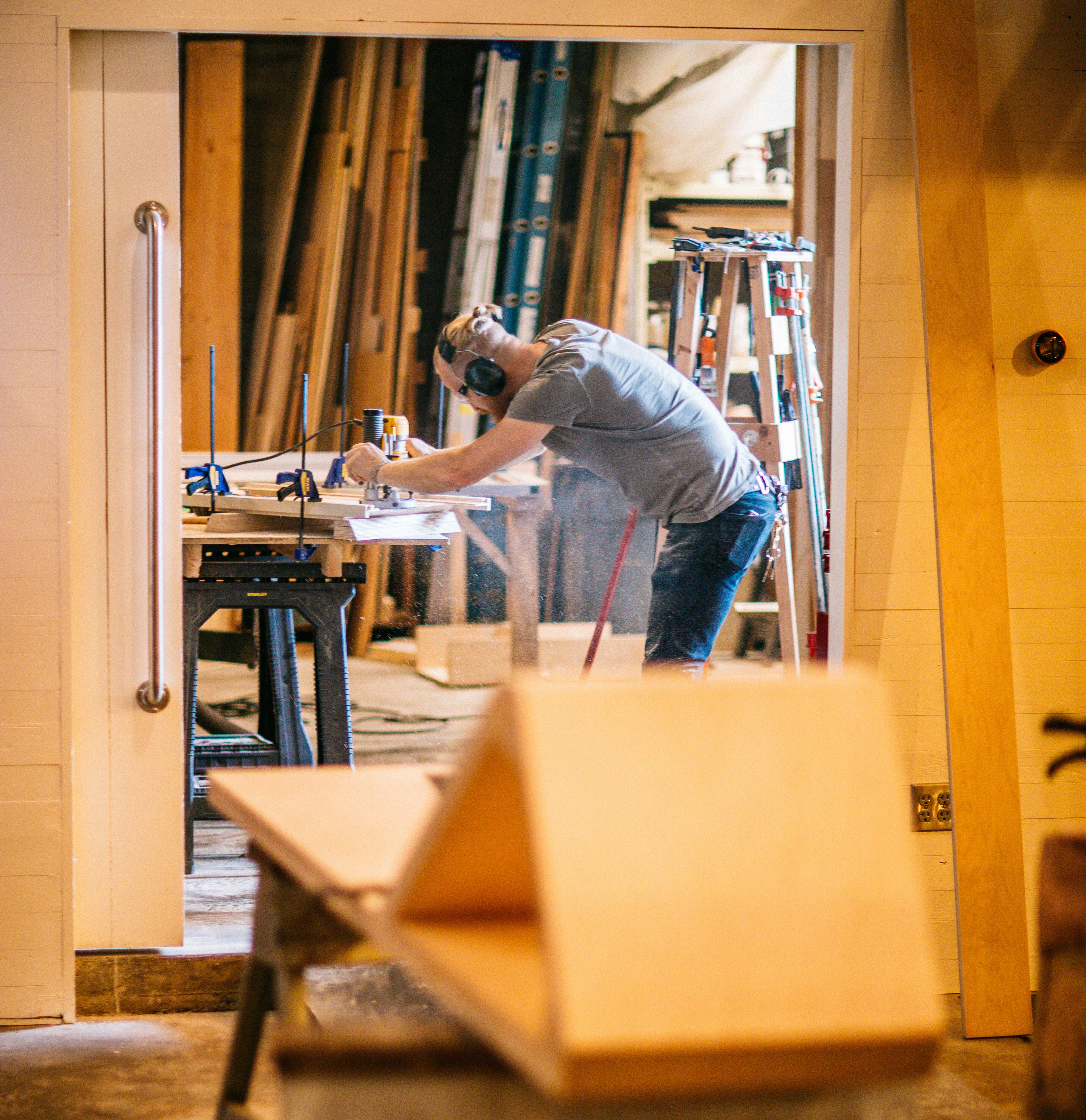 Craftsman bending over a workbench in a Drawn woodworking shop full of lumber and tools
