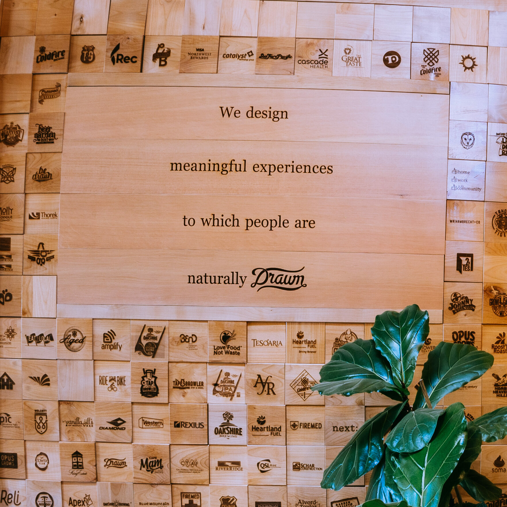 Wood-block wall of branded client logos around a sign reading We design meaningful experiences to which people are naturally