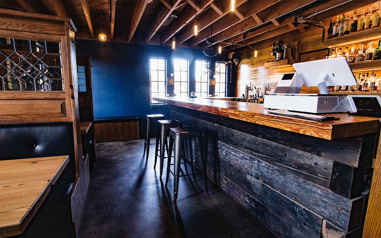 Drawn-designed bar interior with live-edge wood counter, stools and blue accent wall