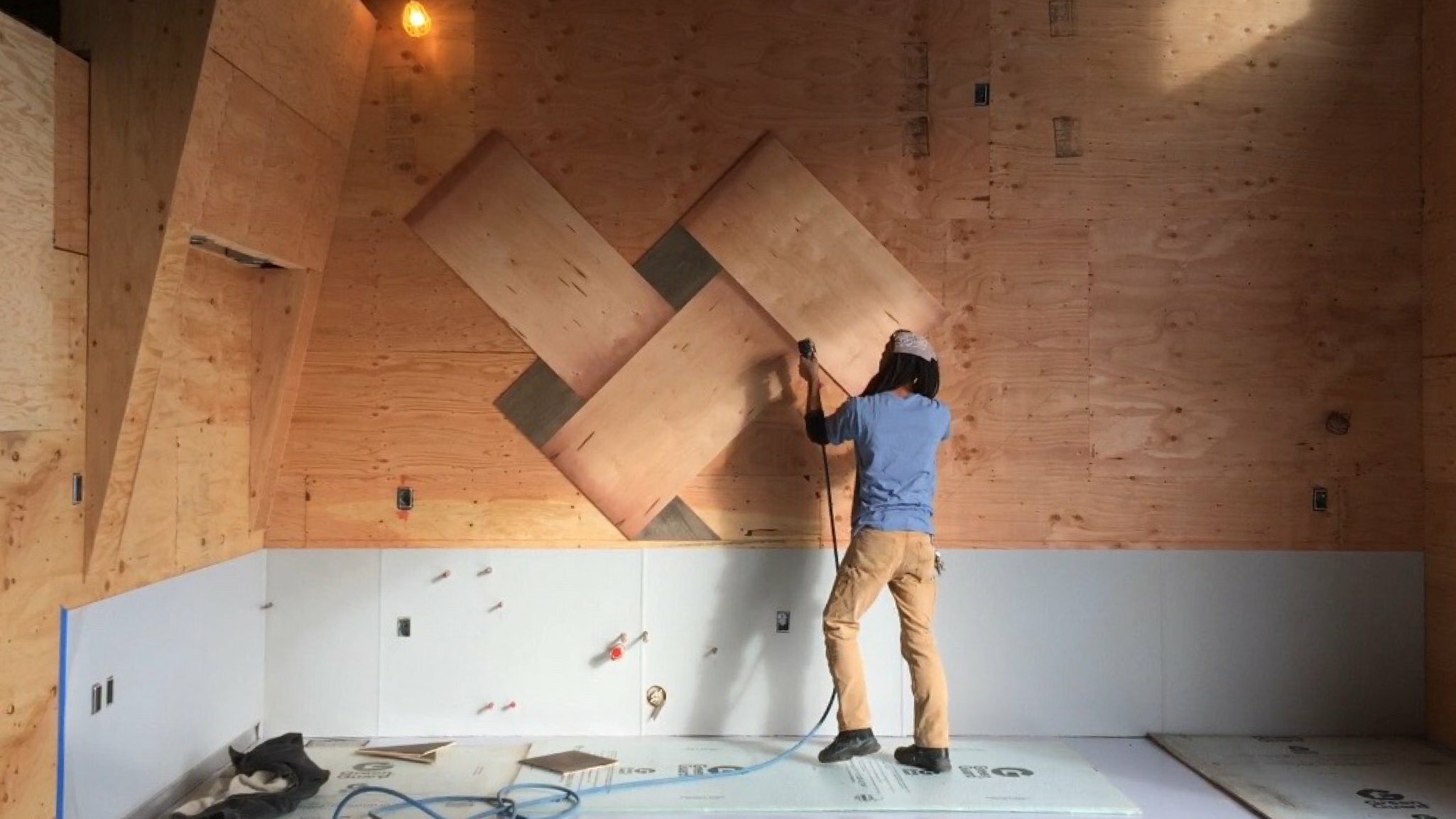 Worker installing a diamond-pattern plywood feature wall during ColdFire taproom construction