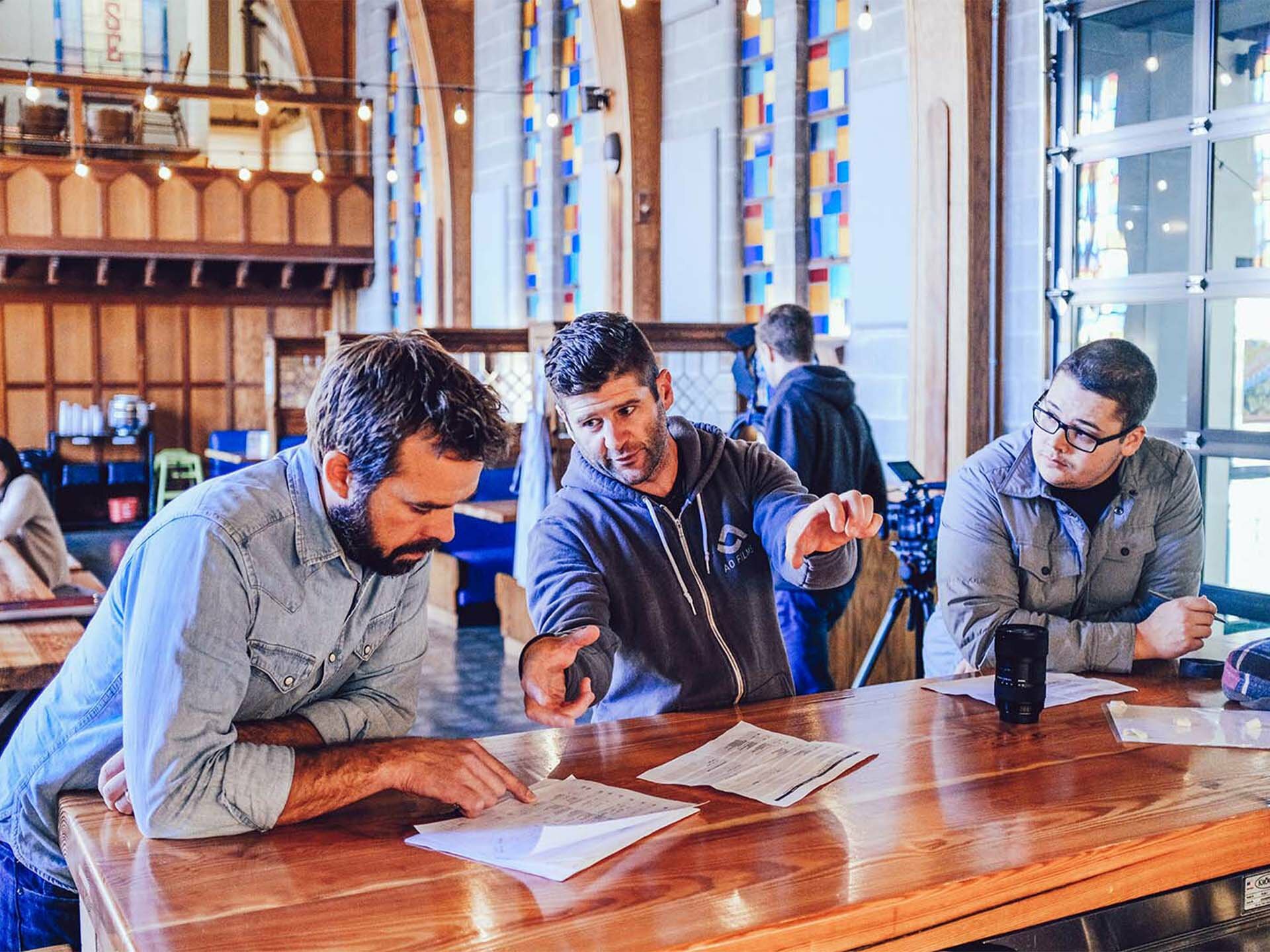 Three men reviewing paperwork at a wood table in a brewery taproom