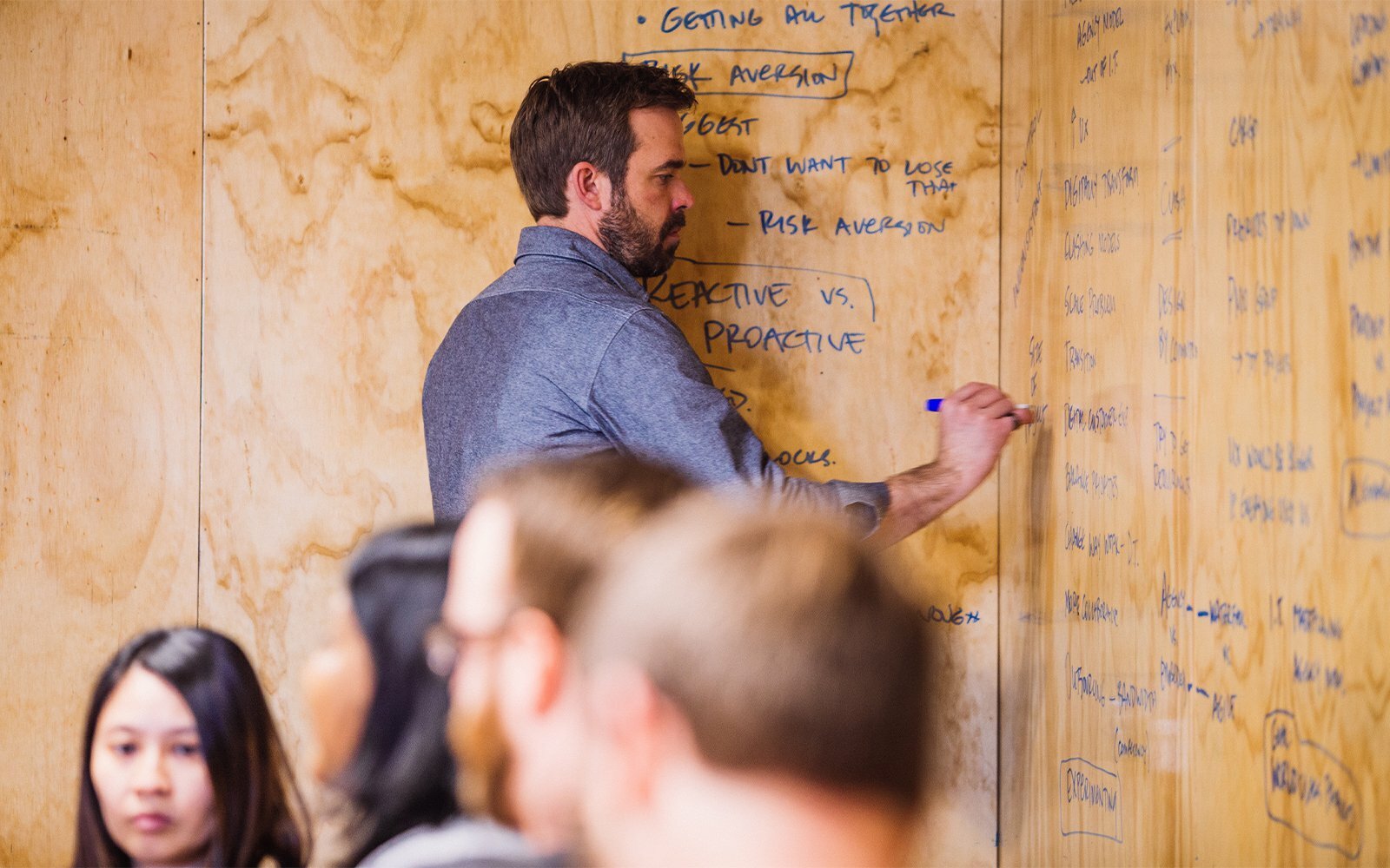 Man brainstorming notes on a plywood wall covered in handwritten ideas during a workshop