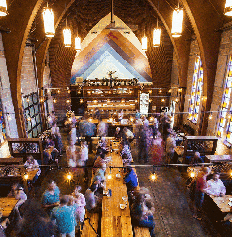 Crowd gathered under arches and string lights in a converted church public house, overhead view