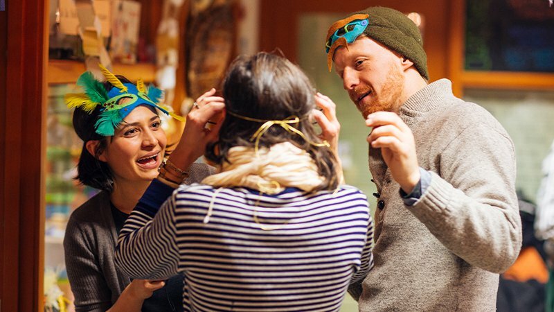 Drawn team members laughing while trying on feathered masquerade masks at a holiday gathering