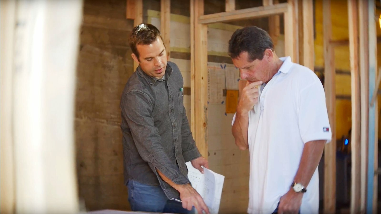 Two men reviewing rolled construction plans inside a building under renovation with exposed framing