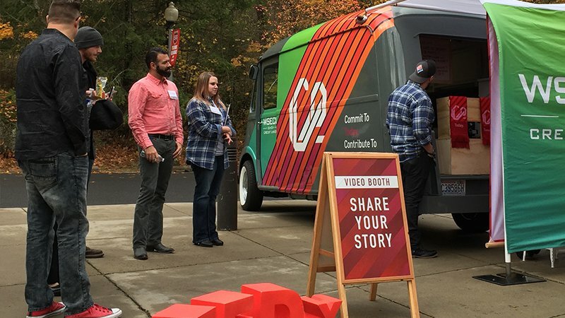 WSECU branded van with a 'Share Your Story' video booth sign and people gathered at an outdoor event