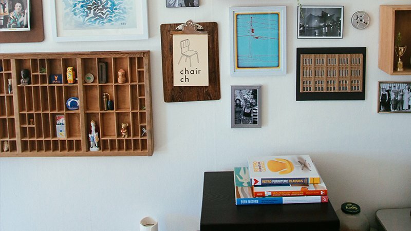 Gallery wall with framed art, a printer's tray of trinkets, a 'chair ch' print, and stacked design books
