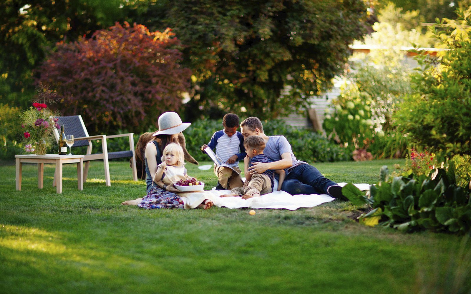 Family reading a book together on a picnic blanket in a green backyard garden
