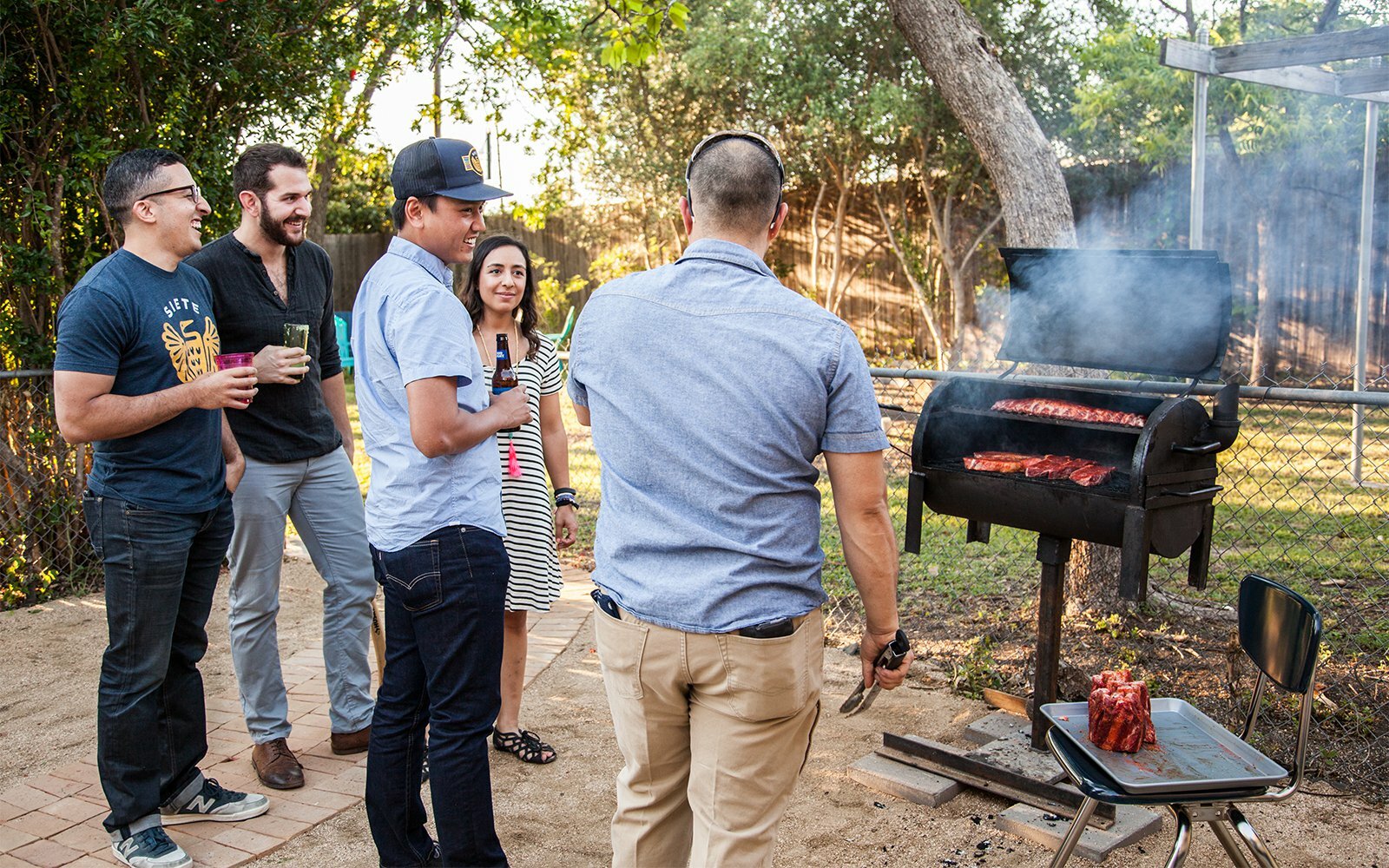 Siete team gathered around a backyard barbecue smoker, drinks in hand at golden hour