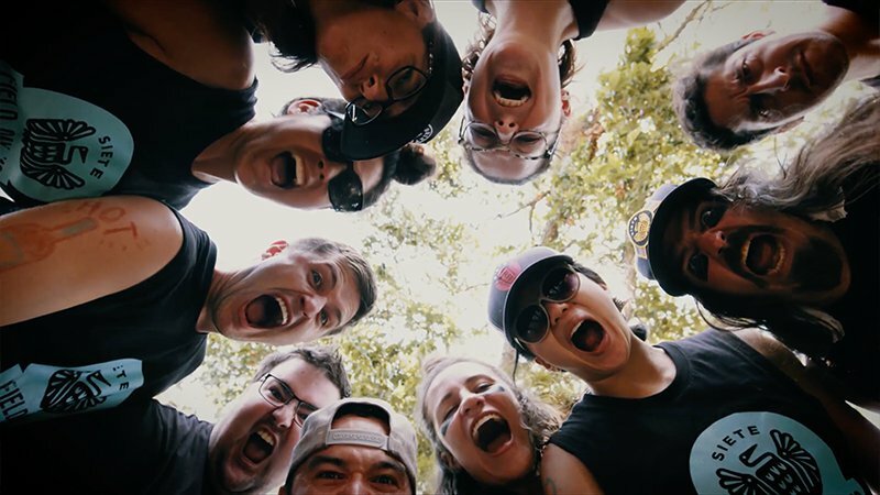 Siete team in a joyful huddle photographed from below with branded caps and tees