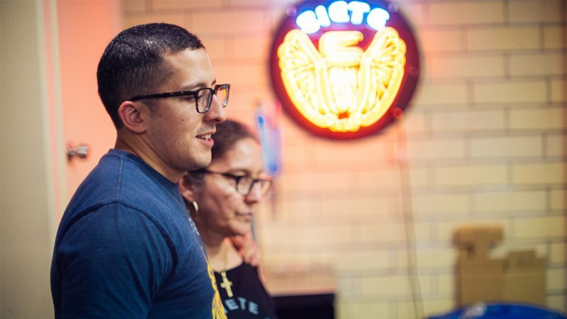Siete team members in conversation beneath a glowing neon Siete eagle sign on brick