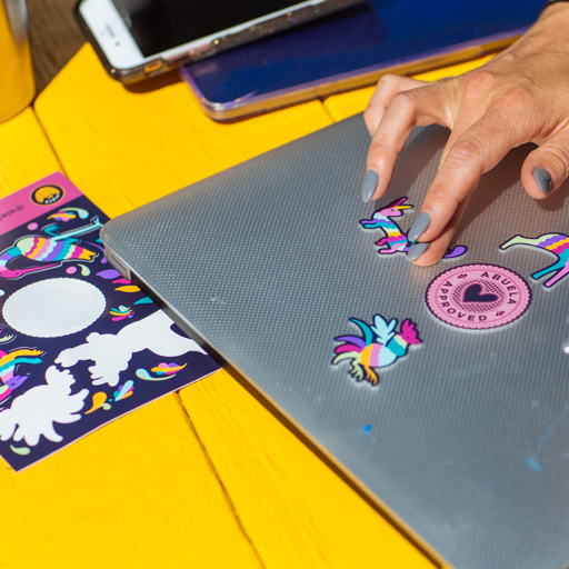 Hand placing colorful Siete unicorn and Abuela Approved stickers on a laptop