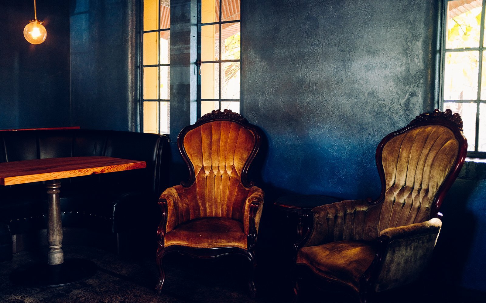 Two ornate vintage upholstered armchairs by a window in a dim moody room