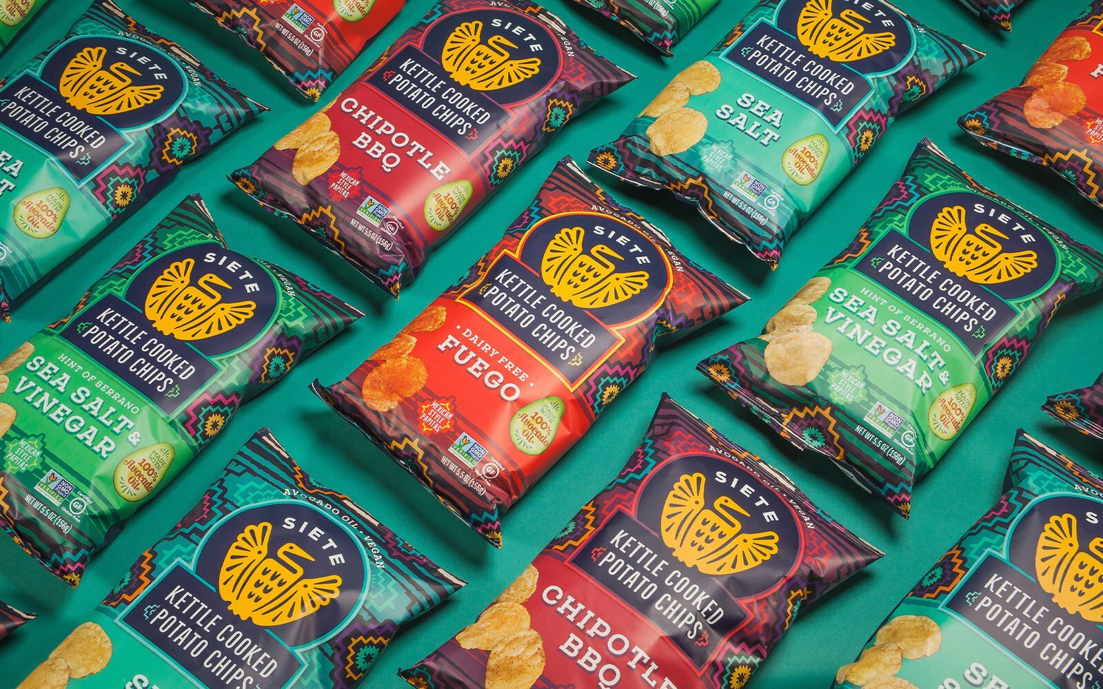 Bags of Siete Kettle Cooked Potato Chips in several flavors arranged on a green surface