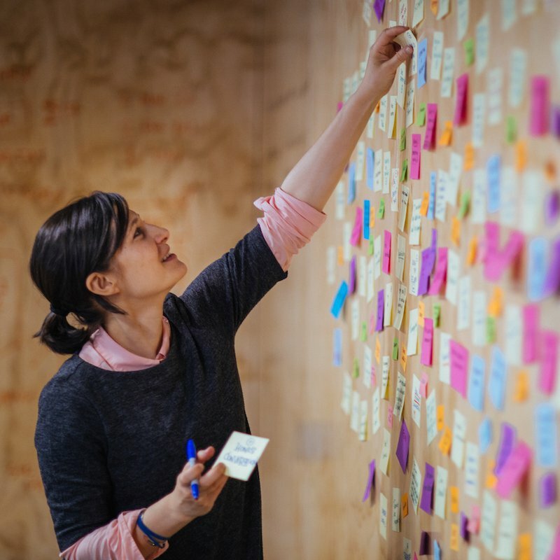 Woman placing colored sticky notes on a plywood ideation wall during a design thinking session