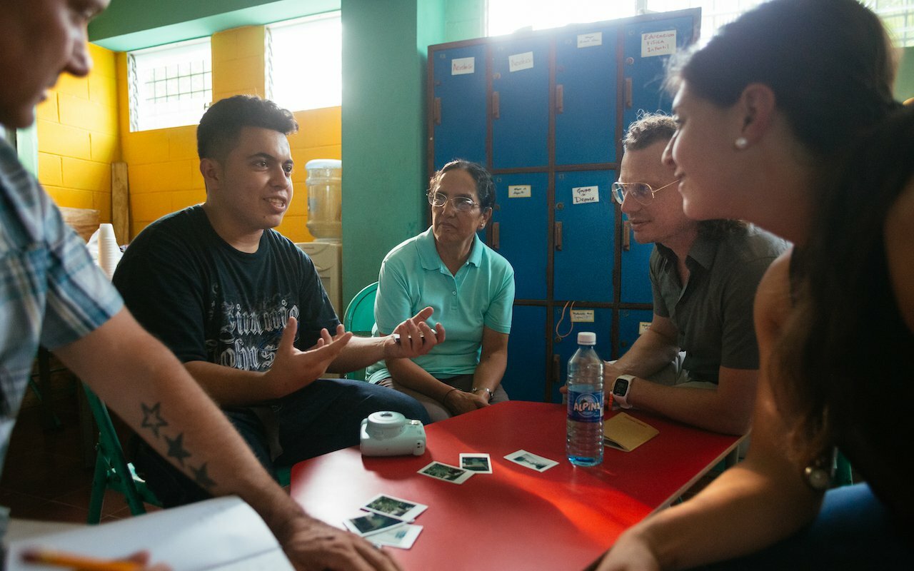 Drawn team and locals talking around a red table during community research in El Salvador
