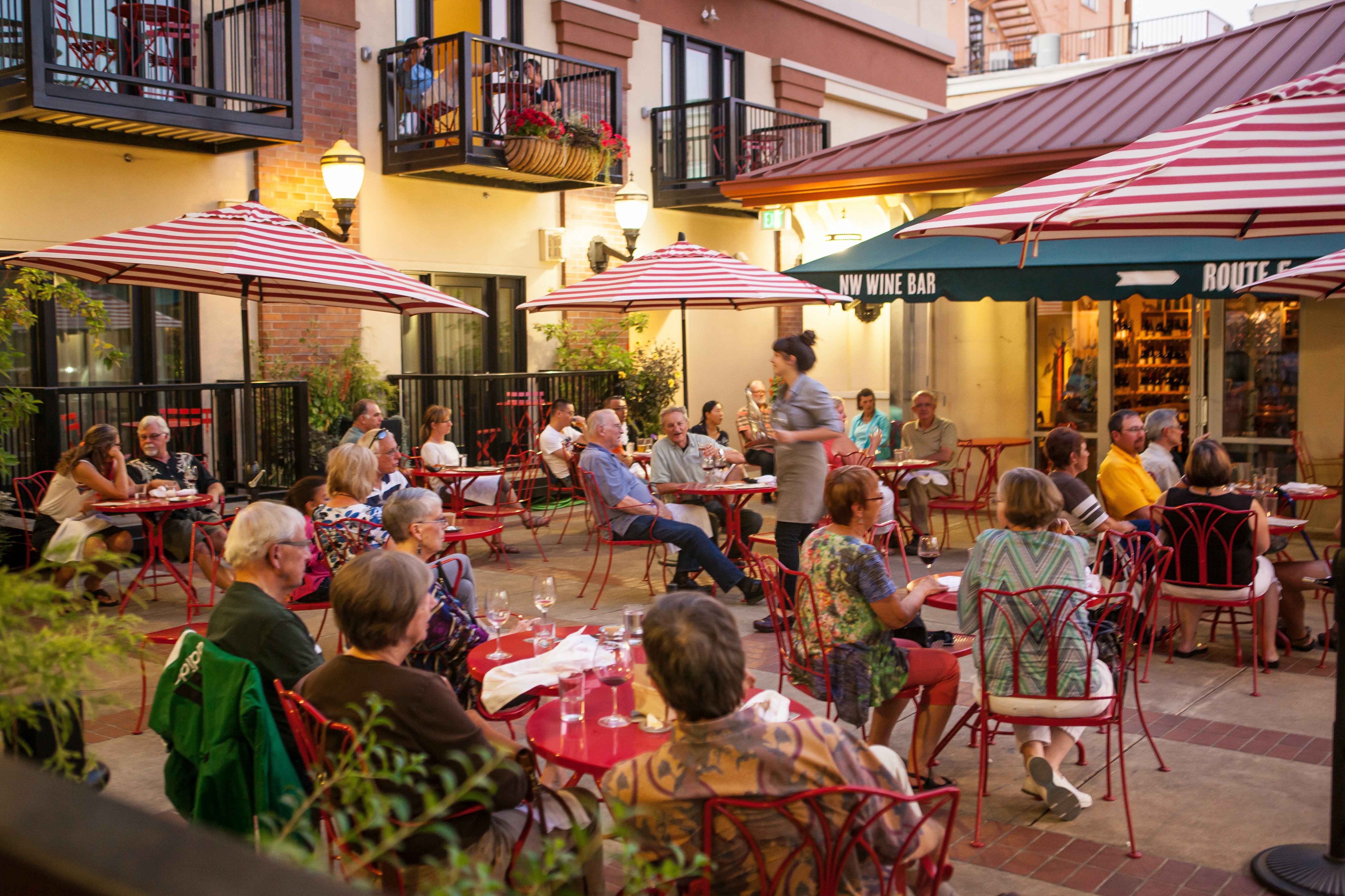 Evening crowd dining under red-striped umbrellas at 5th Street Market courtyard wine bar