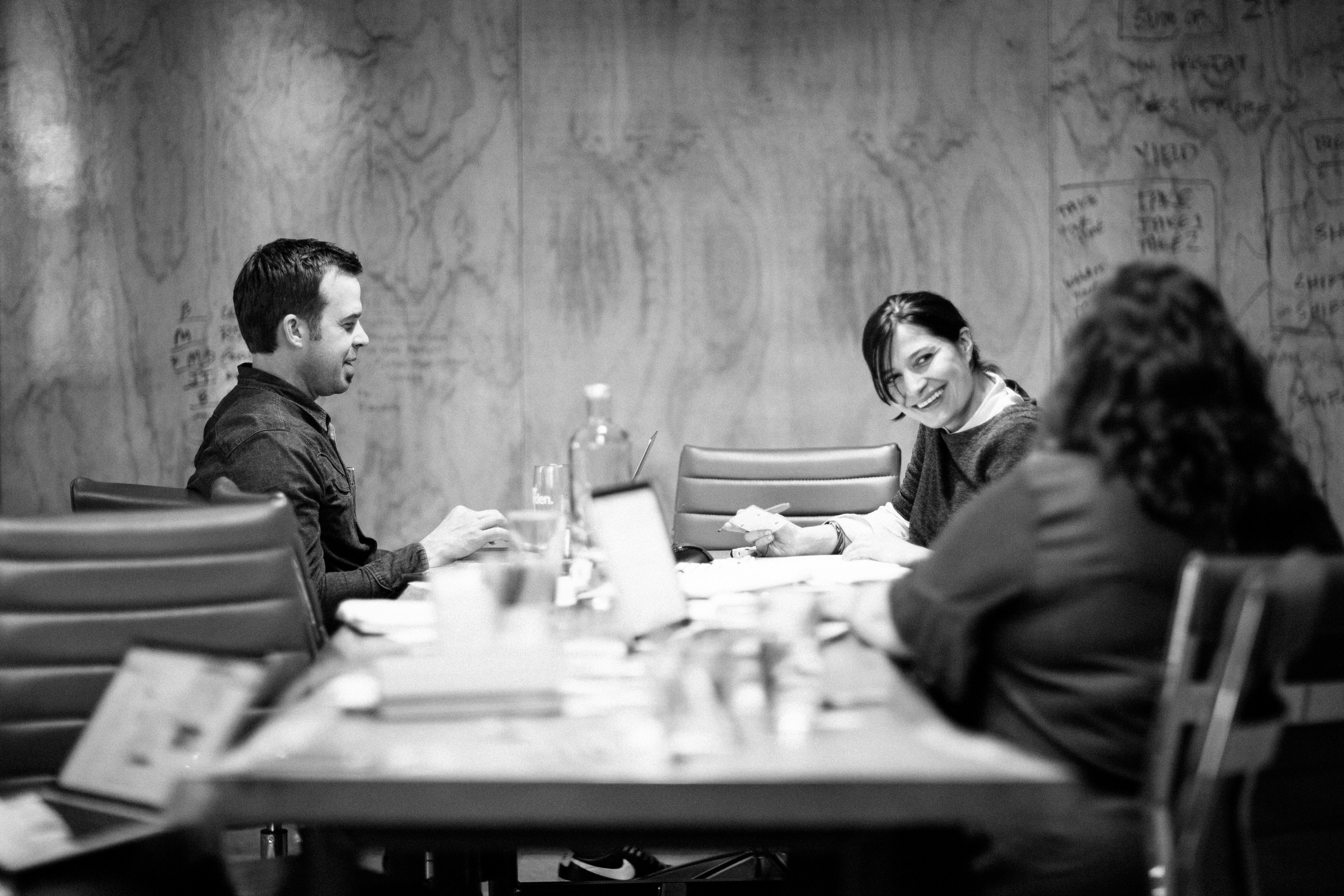Black-and-white photo of Drawn team members meeting around a table against a wood-grain wall