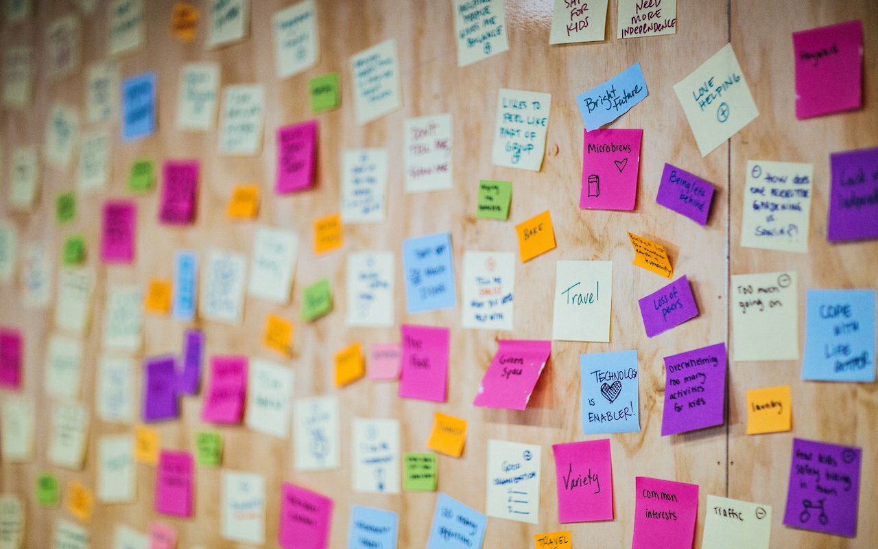 Plywood wall covered in colorful handwritten sticky notes from an ideation session
