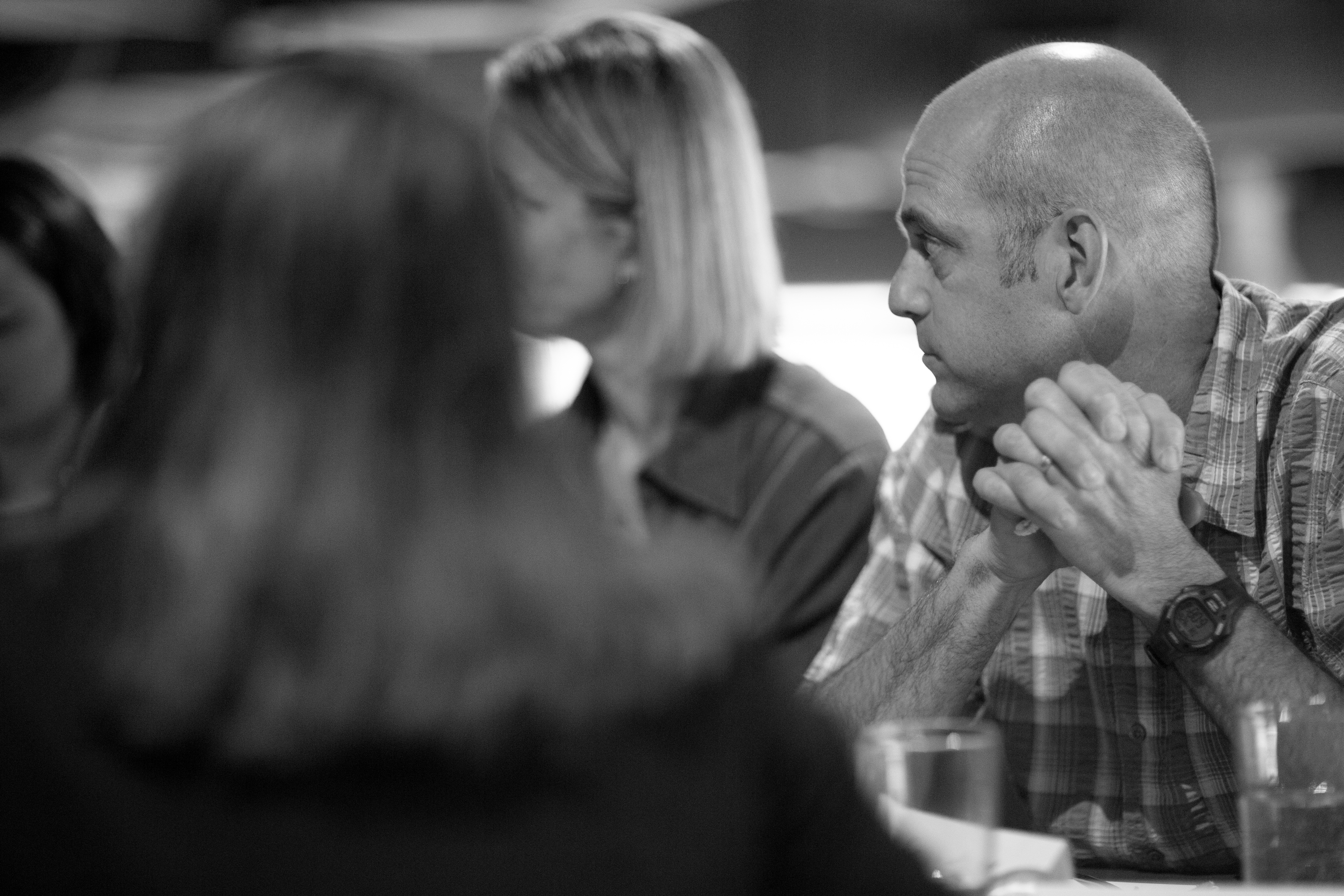 Man listening intently with hands clasped during a group conversation, black-and-white
