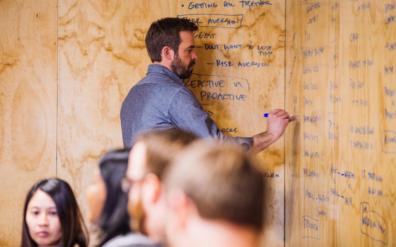 Man brainstorming notes on a plywood wall covered in handwritten ideas during a workshop