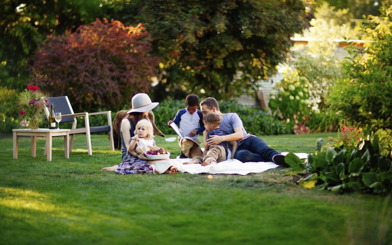 Family reading a book together on a picnic blanket in a green backyard garden