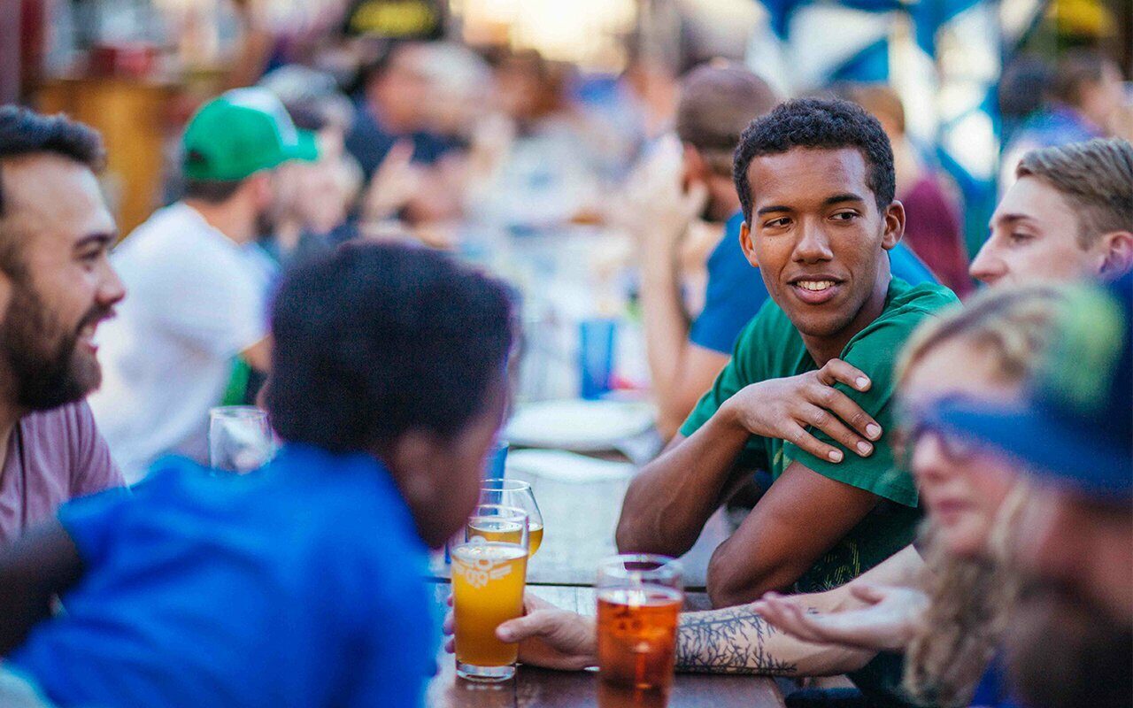 Friends laughing over beers at a crowded outdoor beer garden table at sunset