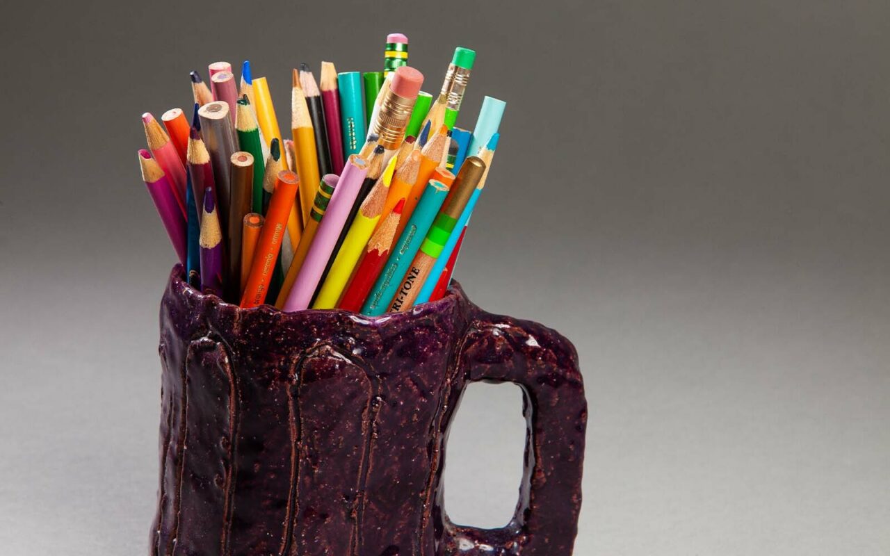 Handmade glossy purple ceramic mug holding a bunch of colored pencils