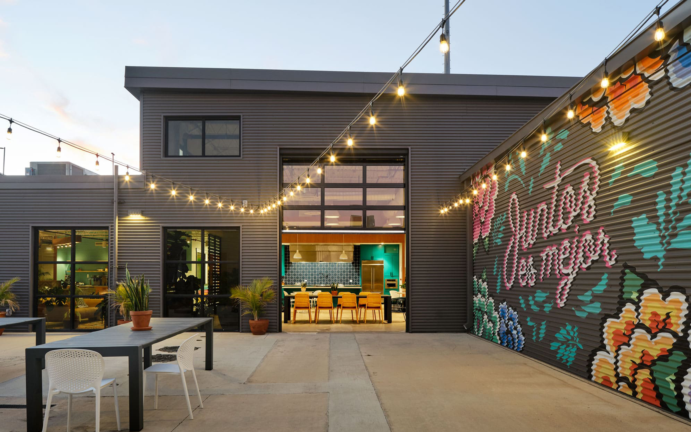 Siete headquarters courtyard at dusk with string lights and a floral 'Juntos es mejor' mural