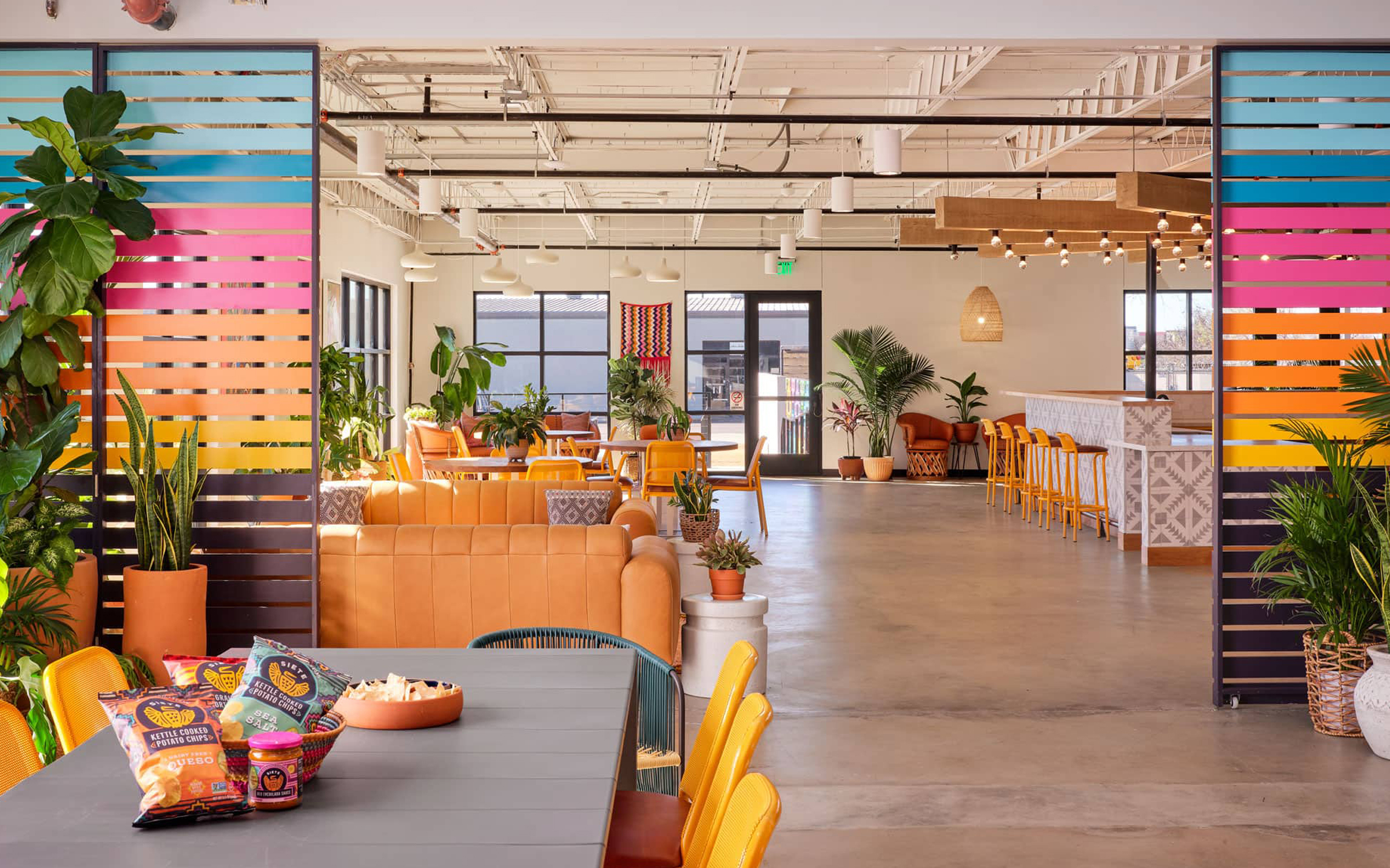 Open Siete office with rainbow slat dividers, orange seating and snack bags on a meeting table