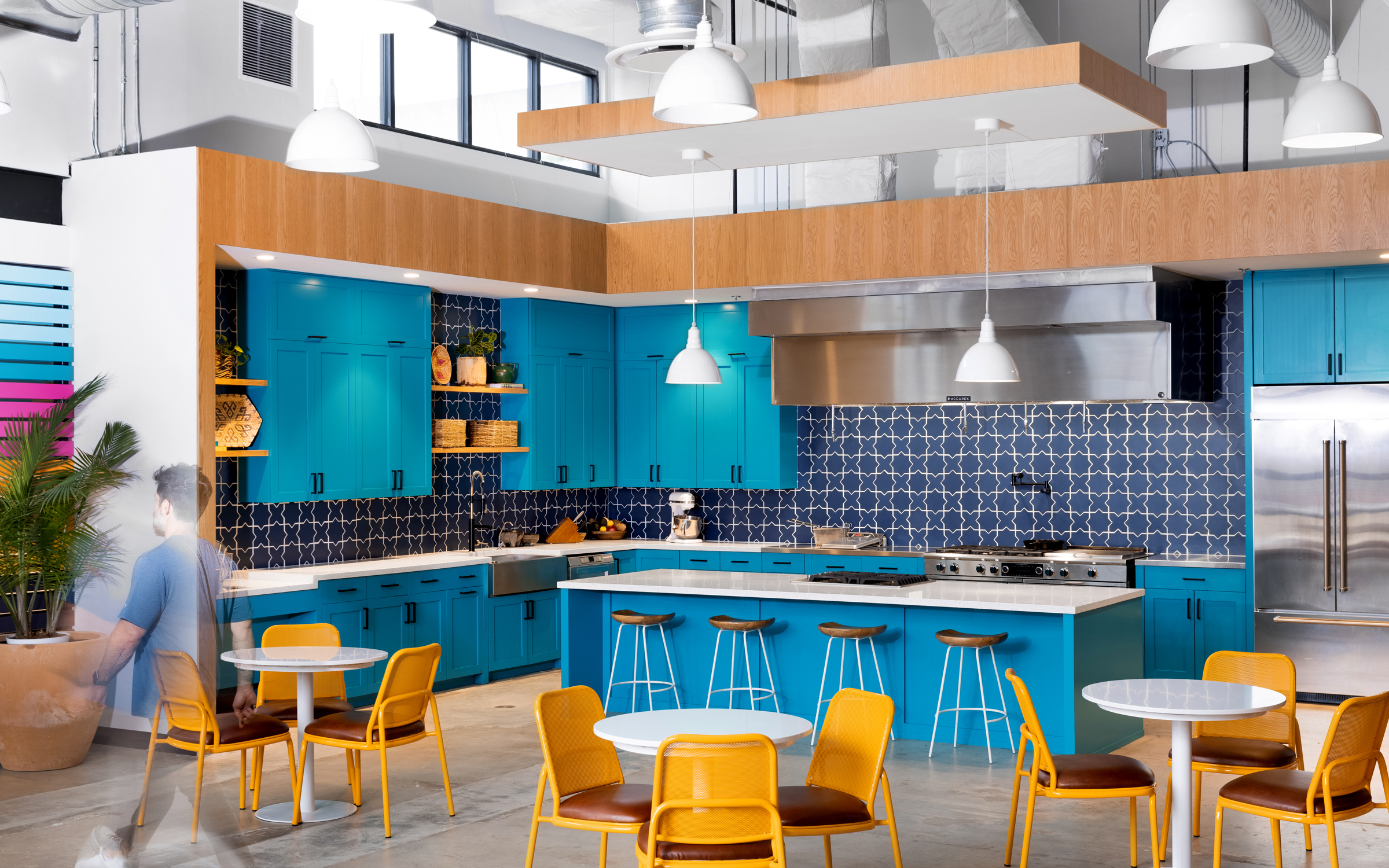 Siete office kitchen with bright blue cabinets, patterned tile, island seating and yellow chairs