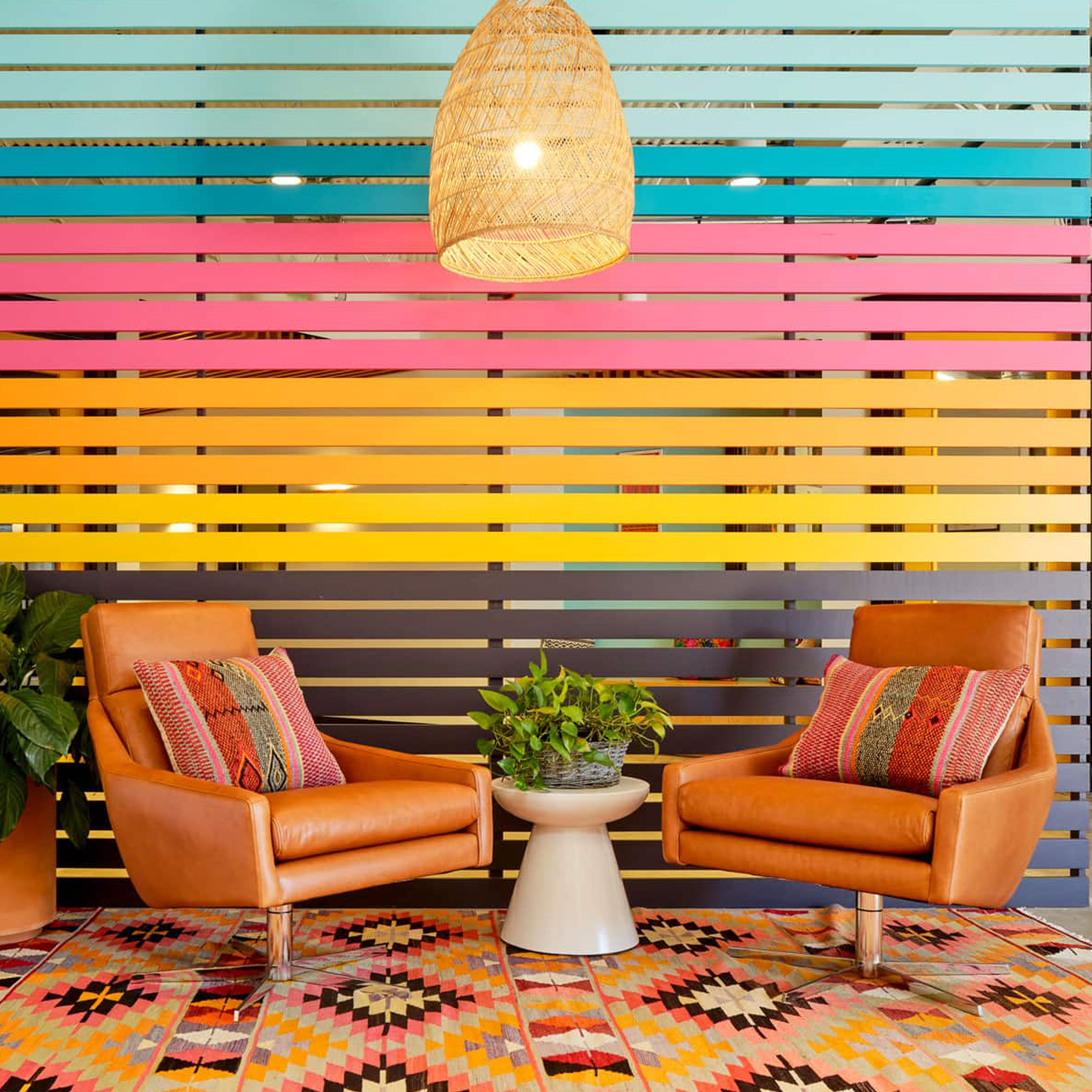 Siete office seating with leather armchairs against a rainbow slat wall over a patterned kilim rug
