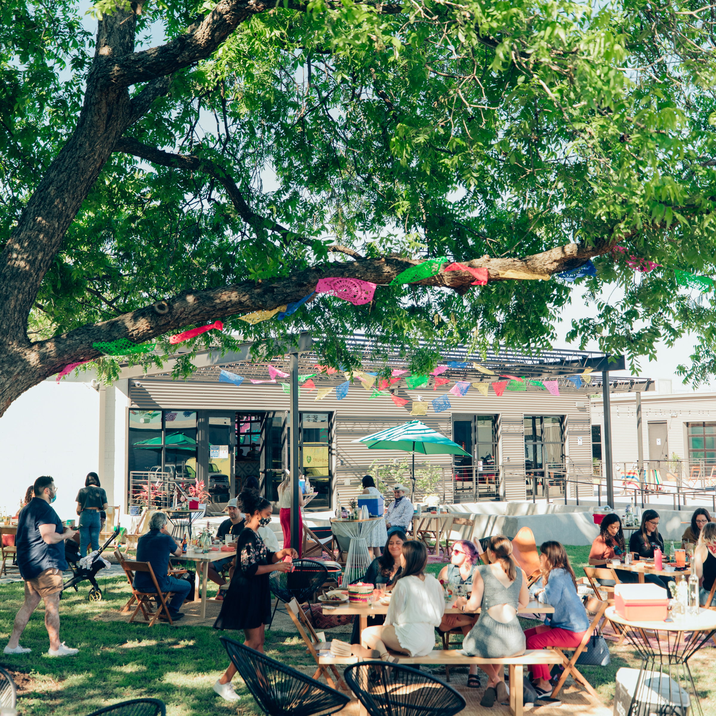 Guests dining outdoors under a tree strung with papel picado at the Siete headquarters patio